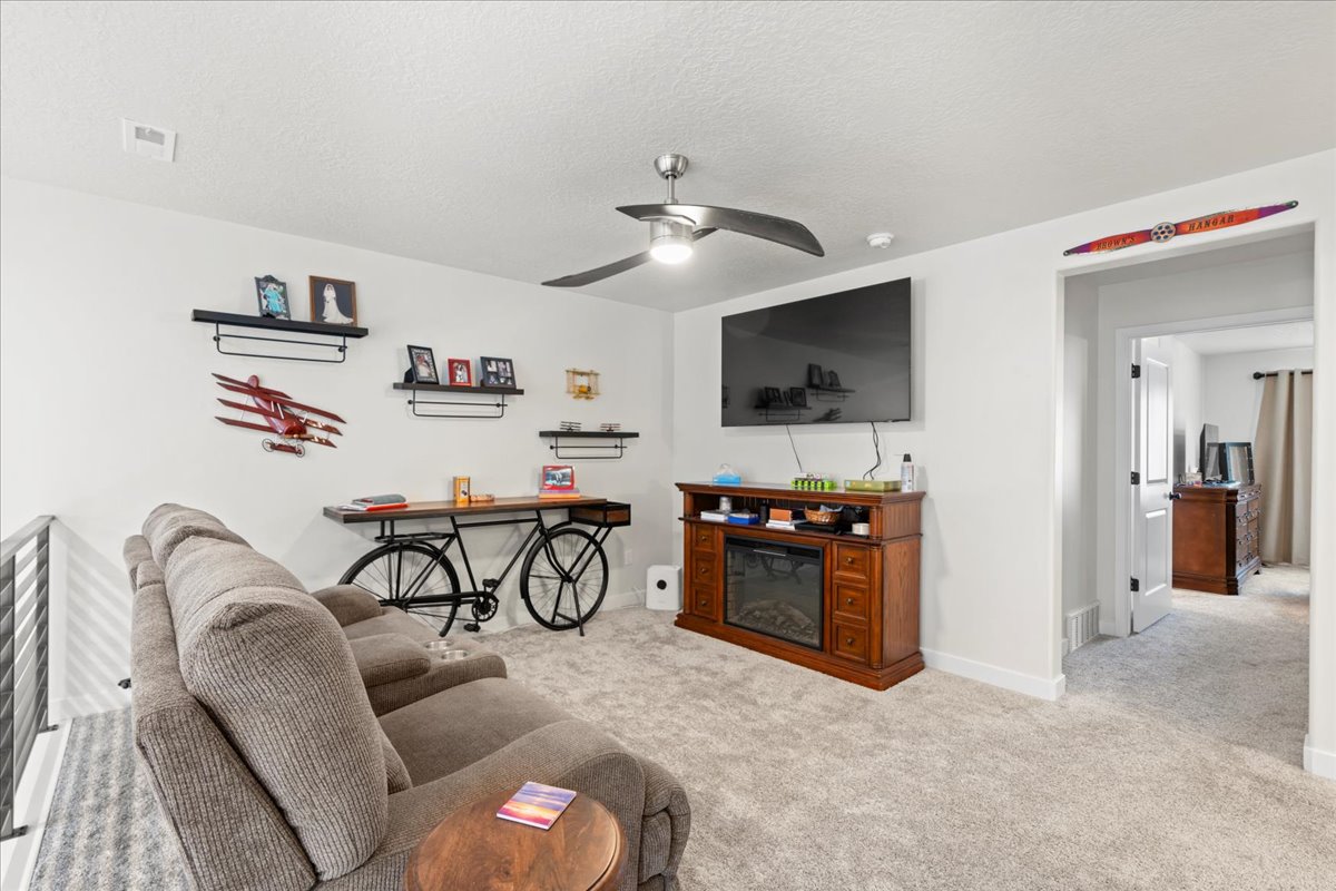 Living area with ceiling fan, light colored carpet, a glass covered fireplace, and a textured ceiling