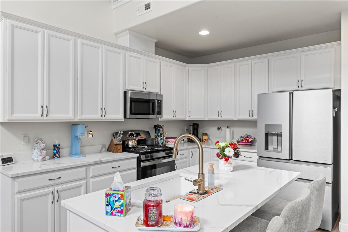 Kitchen featuring stainless steel appliances, white cabinets, a center island with sink, a breakfast bar, and light stone counters
