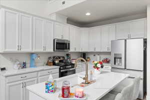 Kitchen featuring stainless steel appliances, white cabinets, a center island with sink, a breakfast bar, and light stone counters