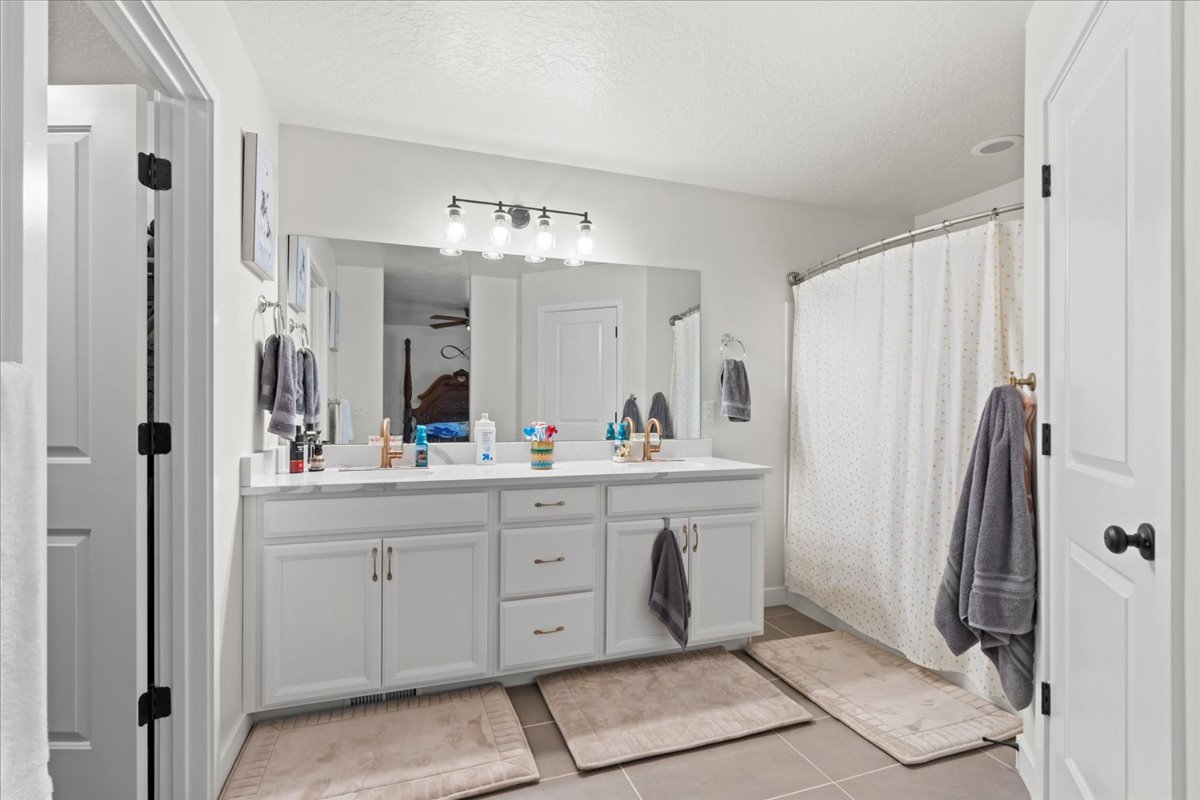 Full bathroom with double vanity, a shower with curtain, a textured ceiling, and light tile patterned floors