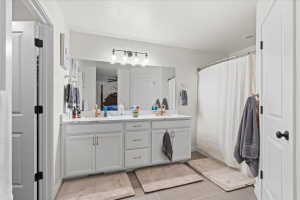 Full bathroom with double vanity, a shower with curtain, a textured ceiling, and light tile patterned floors
