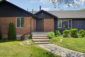 View of front of property featuring a front lawn, brick siding, a shingled roof, and board and batten siding
