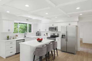 Kitchen featuring stainless steel appliances, white cabinets, light wood-style flooring, recessed lighting, and a kitchen bar