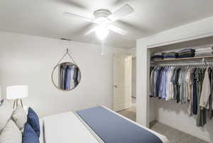 Bedroom with a closet, light colored carpet, a textured ceiling, and a ceiling fan