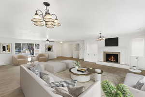Living area with a chandelier, ceiling fan, light wood-style flooring, and a warm lit fireplace
