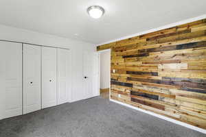 Unfurnished bedroom featuring wood walls, carpet flooring, crown molding, and a closet