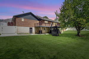 Back of house at dusk featuring a gate, brick siding, a wooden deck, and a chimney