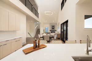 Kitchen with light stone countertops, a high ceiling, light wood finish cabinetry, modern cabinets, and a large fireplace