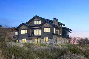 Back of house with stone siding and a chimney
