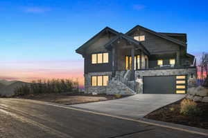 View of front of property featuring stone siding, driveway, and an attached garage