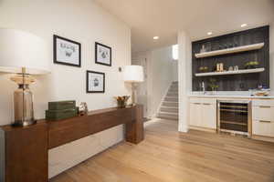 Indoor wet bar with open shelves, light wood-type flooring, beverage cooler, recessed lighting, and light countertops