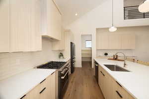Kitchen featuring light wood finish cabinets, vaulted ceiling, stainless steel appliances, modern cabinets, and light stone countertops
