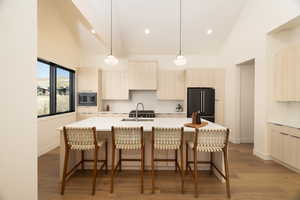 Kitchen featuring light wood finish cabinets, vaulted ceiling, hanging light fixtures, light wood-style flooring, and backsplash