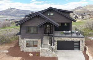 View of front of home with a mountain view, driveway, stone siding, a balcony, and an attached garage