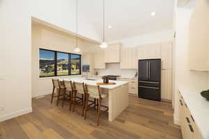 Kitchen featuring high quality fridge, light wood finish cabinetry, a kitchen island with sink, decorative light fixtures, and a kitchen breakfast bar
