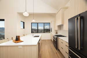 Dual tone kitchen featuring premium appliances, an island with sink, light wood-type flooring, lofted ceiling, and hanging light fixtures