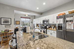 Kitchen featuring stainless steel appliances, white cabinets, light stone counters, a ceiling fan, and recessed lighting