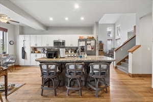 Kitchen featuring white cabinets, stainless steel appliances, light wood-type flooring, a center island with sink, and a breakfast bar area