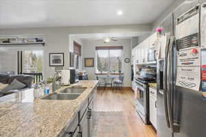 Kitchen with stainless steel appliances, light wood-style flooring, open floor plan, a ceiling fan, and light stone counters