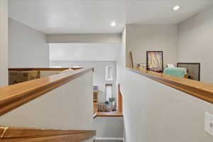 Hallway with a textured wall, recessed lighting, and an upstairs landing
