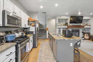 Kitchen featuring open floor plan, stainless steel appliances, a fireplace, light stone countertops, and light wood-style floors