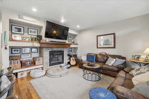 Living room with a tiled fireplace, light wood finished floors, and recessed lighting