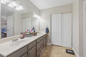 Bathroom with double vanity, light tile patterned floors, and a closet