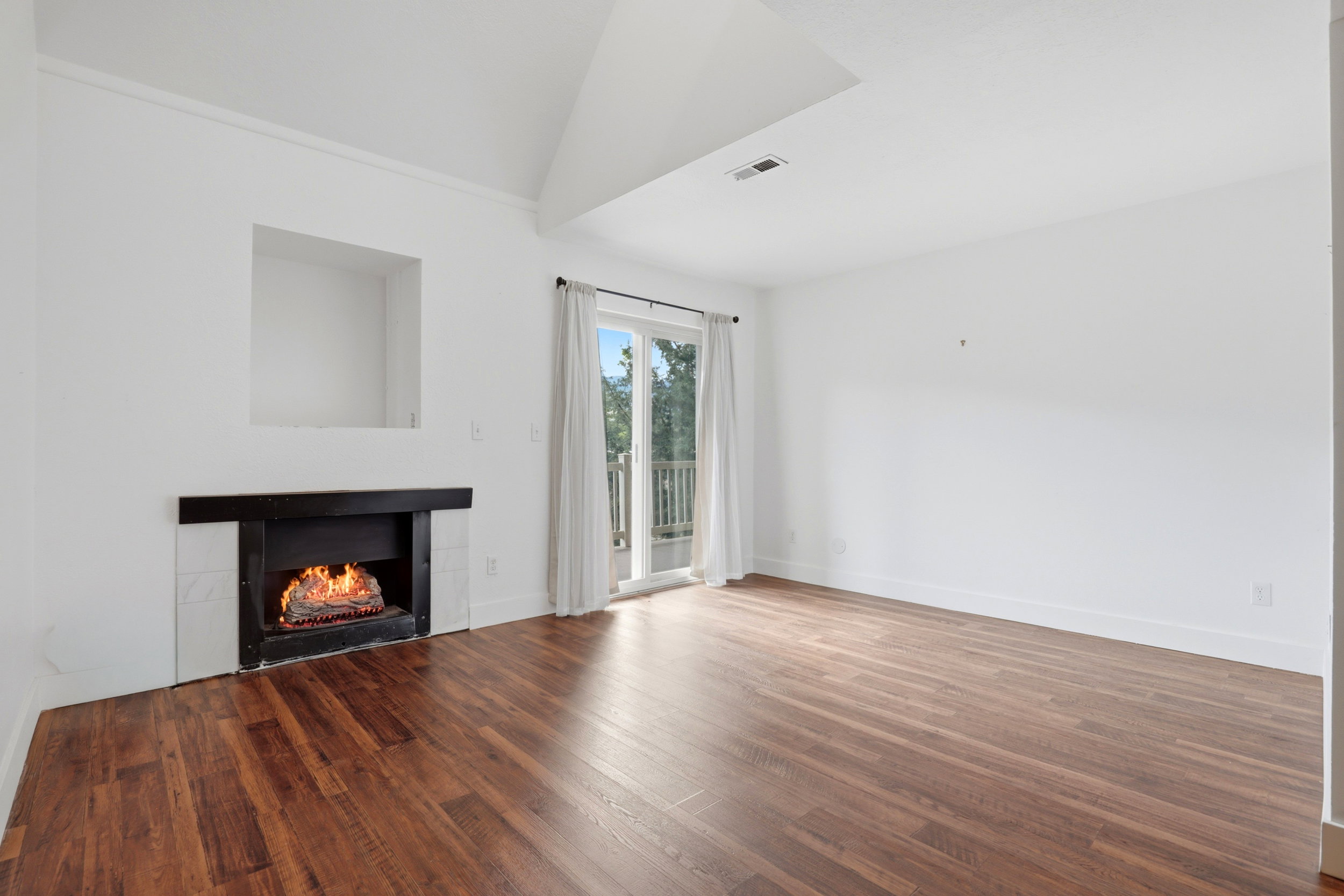 Living area with wood-finish flooring, a fireplace featuring a black mantel and white tile surround, and a recessed wall niche