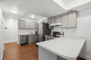 Kitchen featuring grey cabinetry, stainless steel appliances, wood-finish flooring, white countertops, and recessed lighting
