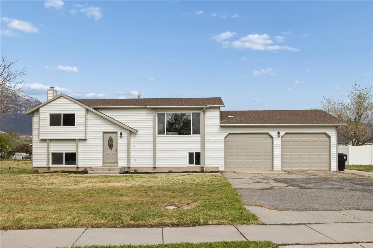 Raised ranch featuring asphalt driveway, a front yard, an attached garage, a chimney, and entry steps