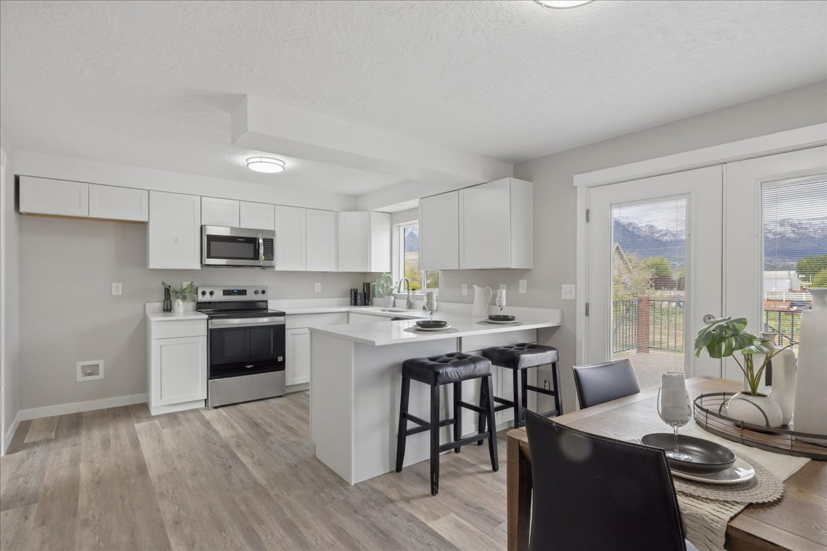 Kitchen with a kitchen bar, stainless steel appliances, white cabinets, a peninsula, and a textured ceiling