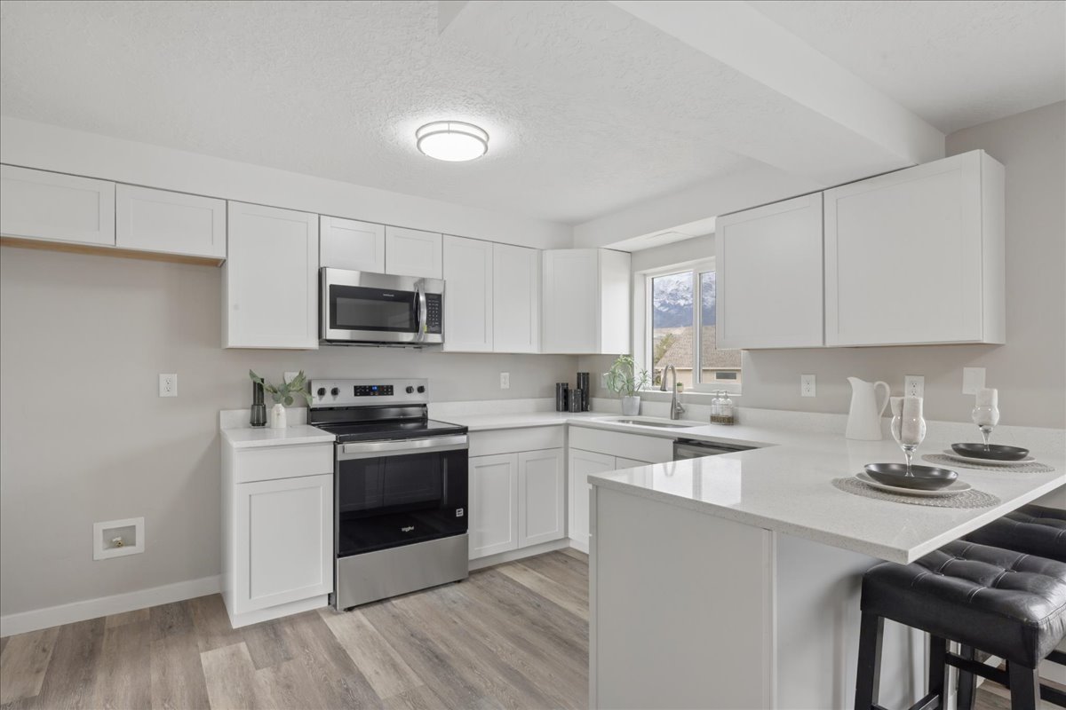 Kitchen with a kitchen bar, stainless steel appliances, a peninsula, white cabinetry, and a textured ceiling