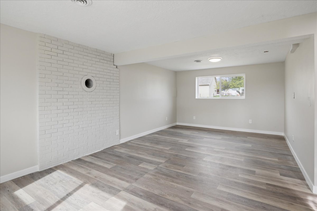 Unfurnished room featuring brick wall, light wood-style floors, and beam ceiling