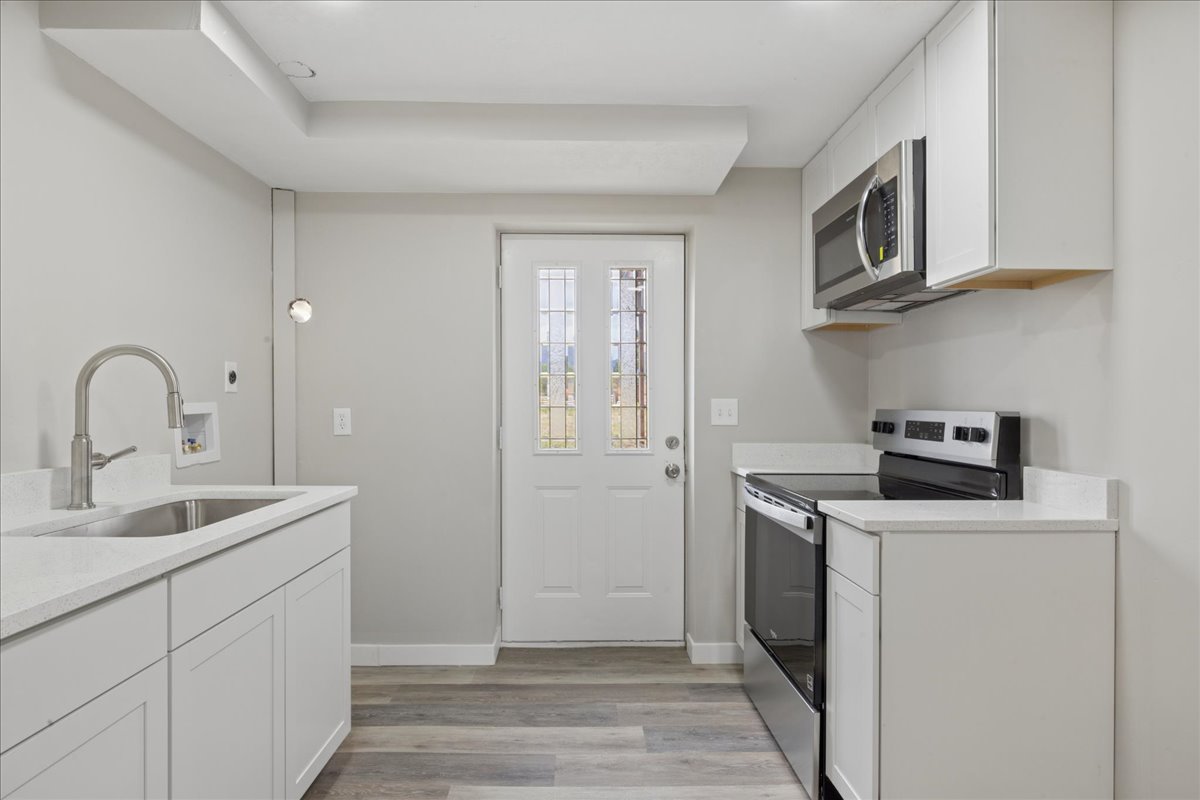 Kitchen with white cabinetry, stainless steel appliances, light stone countertops, and light wood-type flooring
