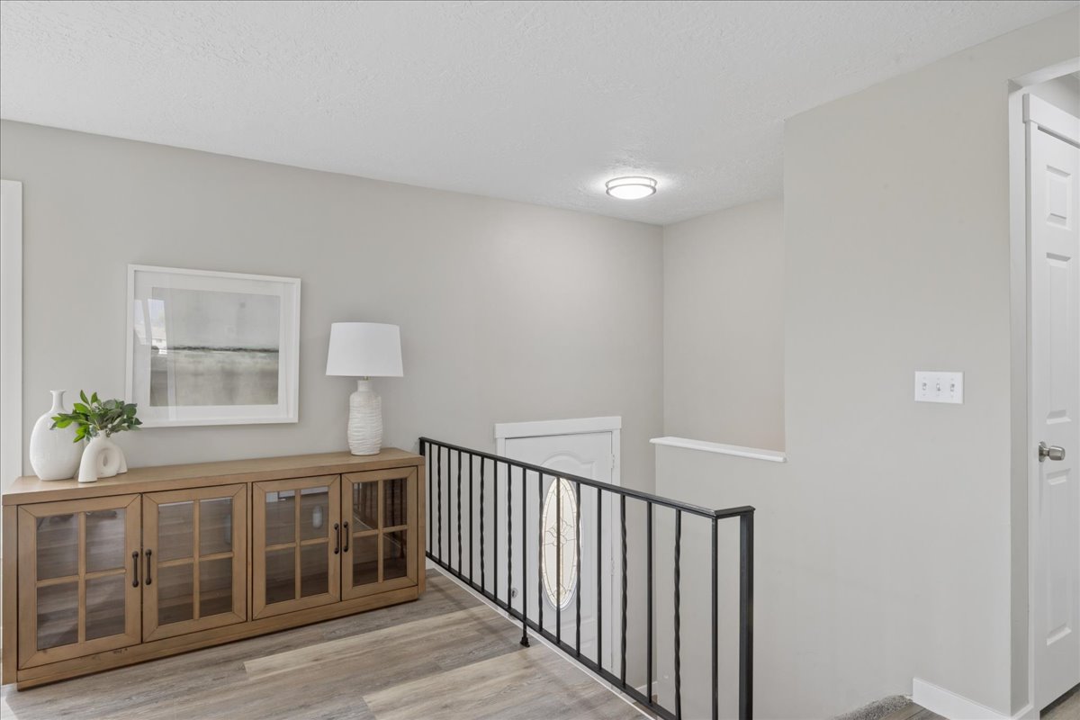 Corridor with light wood-style floors, a textured ceiling, and an upstairs landing