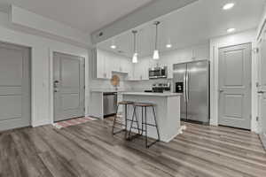 Kitchen featuring stainless steel appliances, a kitchen island, white cabinetry, a kitchen breakfast bar, and decorative light fixtures