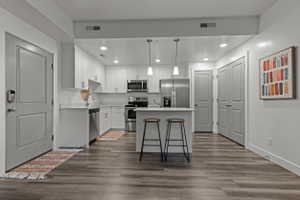 Kitchen featuring light countertops, stainless steel appliances, a center island, white cabinets, and dark wood-style floors