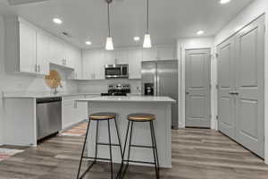 Kitchen featuring stainless steel appliances, a kitchen breakfast bar, a kitchen island, white cabinetry, and light wood-style floors