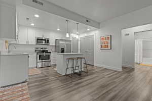 Kitchen with stainless steel appliances, a kitchen island, white cabinets, a kitchen breakfast bar, and light wood finished floors