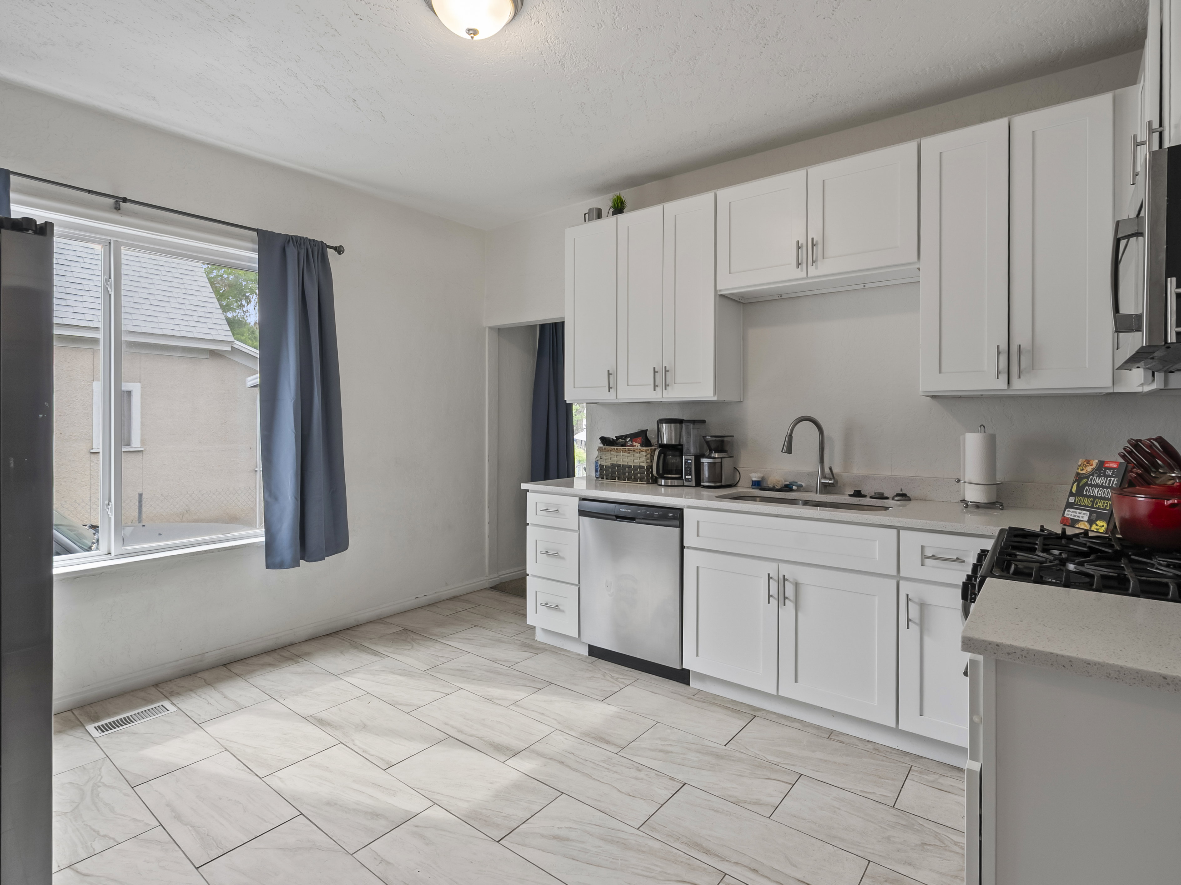 Kitchen with white cabinetry, stainless steel appliances, light stone counters, and a textured ceiling