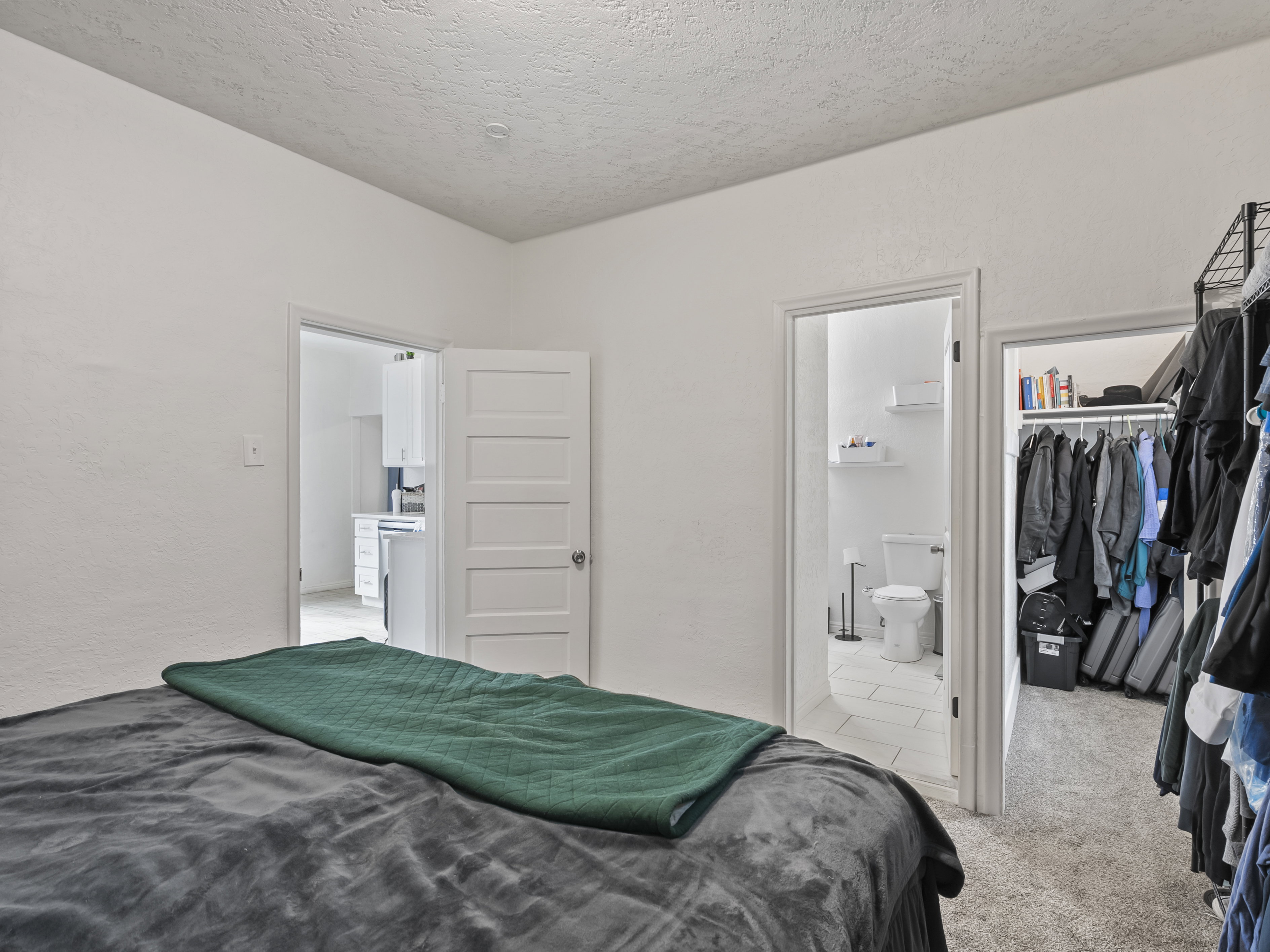 Bedroom with light colored carpet, a textured ceiling, a spacious closet, and a textured wall