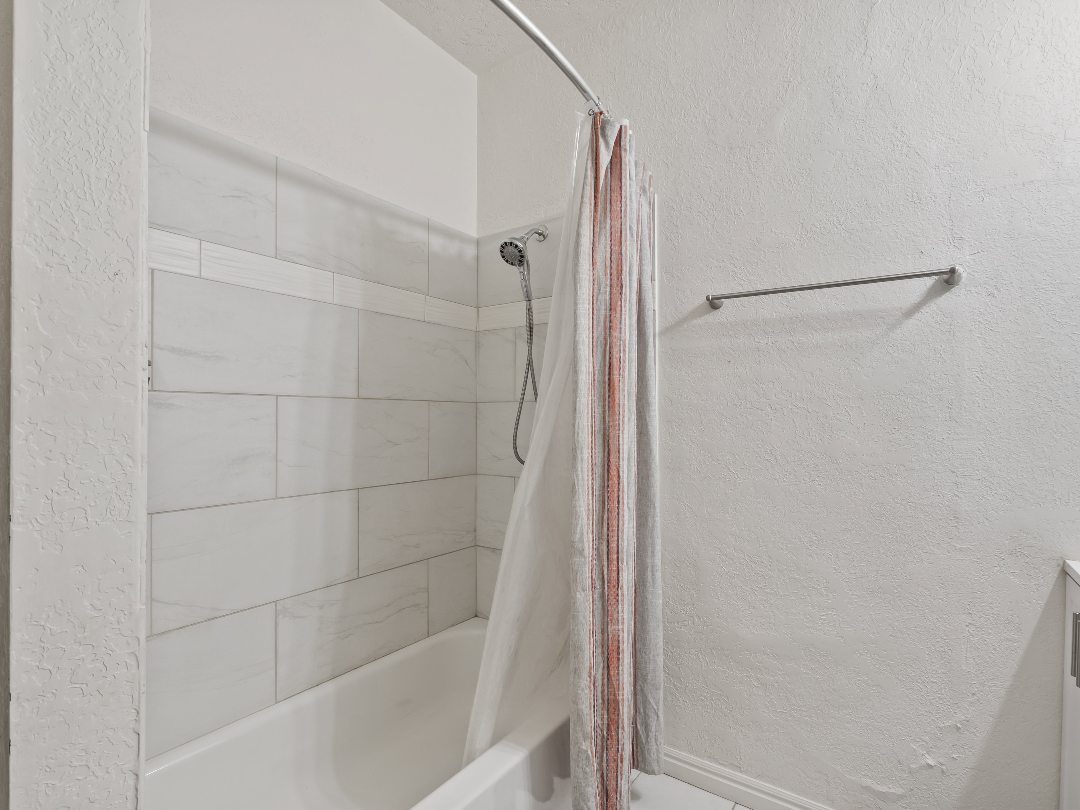 Bathroom with a textured wall, shower / bath combo with shower curtain, and vanity
