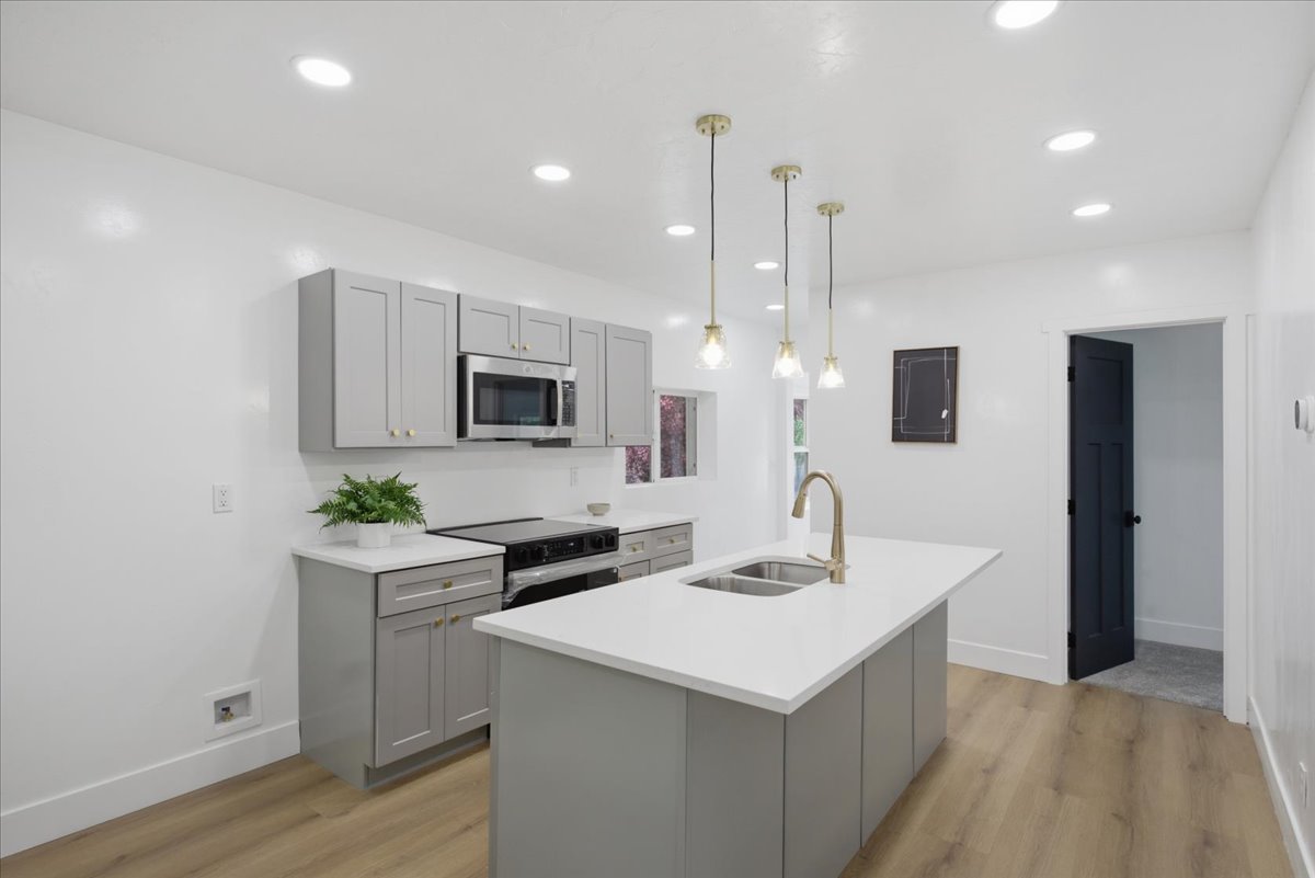 Kitchen featuring gray cabinets, a kitchen island with sink, light wood finished floors, and black range with electric cooktop