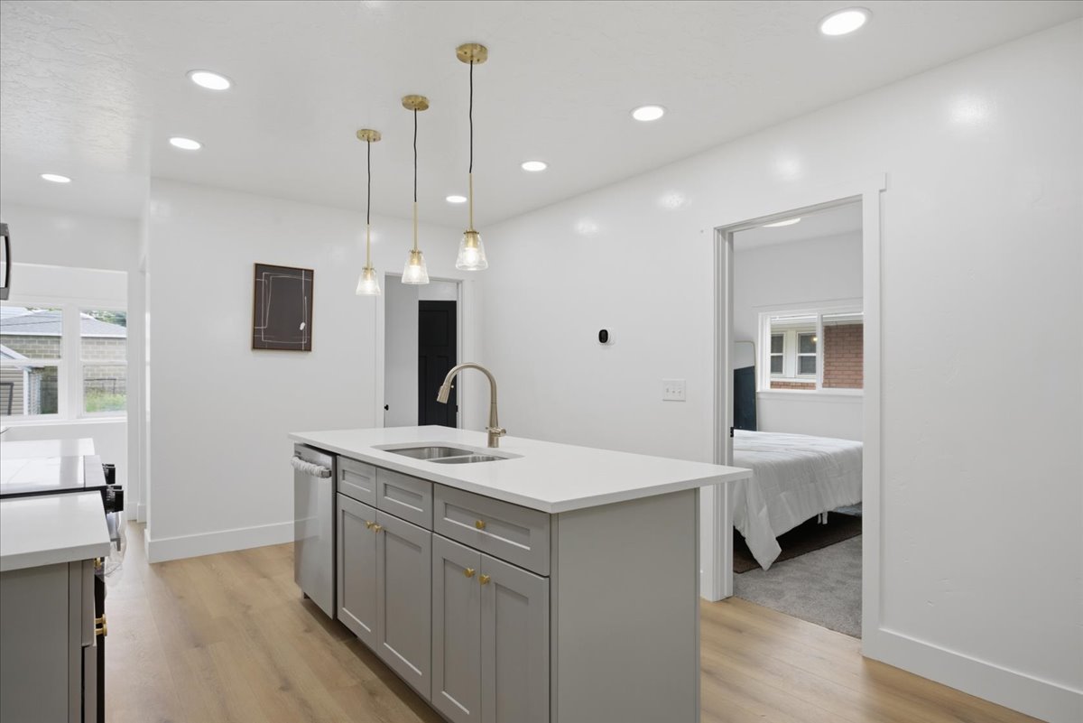 Kitchen with gray cabinets, a center island with sink, decorative light fixtures, light stone counters, and light wood-style flooring