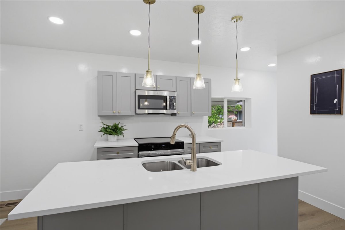 Kitchen with gray cabinetry, light wood finished floors, an island with sink, light stone countertops, and stainless steel microwave