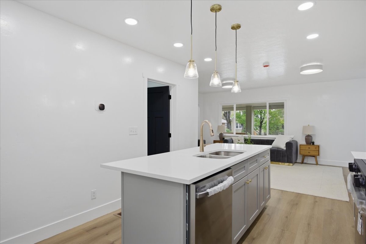 Kitchen featuring a center island with sink, light wood-style flooring, decorative light fixtures, gray cabinetry, and stainless steel appliances