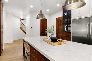 Kitchen with light wood-style floors, a kitchen bar, glass insert cabinets, stainless steel fridge, and light stone counters