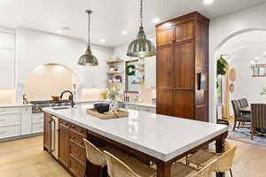 Dual tone kitchen featuring arched walkways, open shelves, a center island with sink, light wood-type flooring, and two tone color scheme