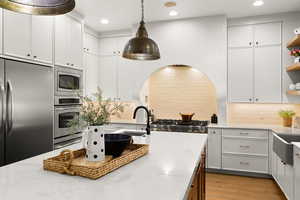 Dual tone kitchen featuring dual tone cabinetry, stainless steel appliances, light wood finished floors, light stone counters, and open shelves