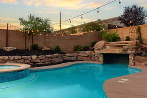 Pool at dusk with a fenced backyard and a pool with connected hot tub